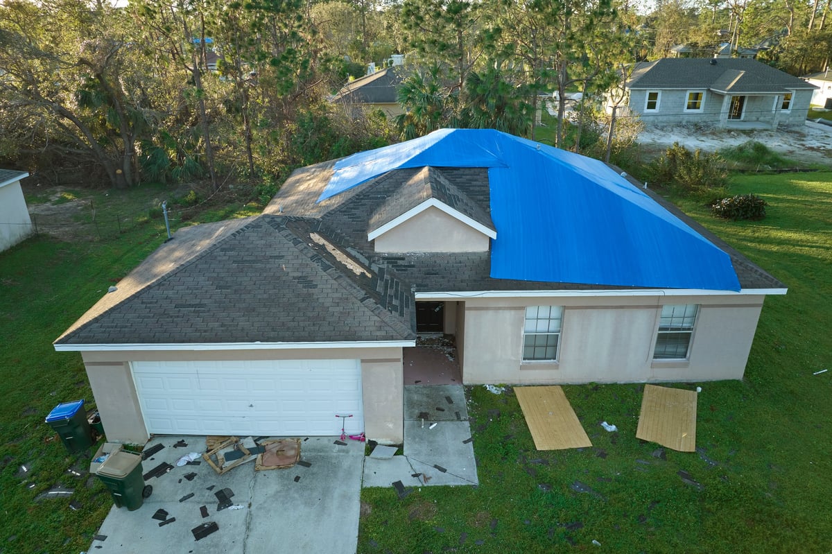 Aerial view of a hurricane-damaged house roof covered with a blue protective tarp to stop rain water leaking