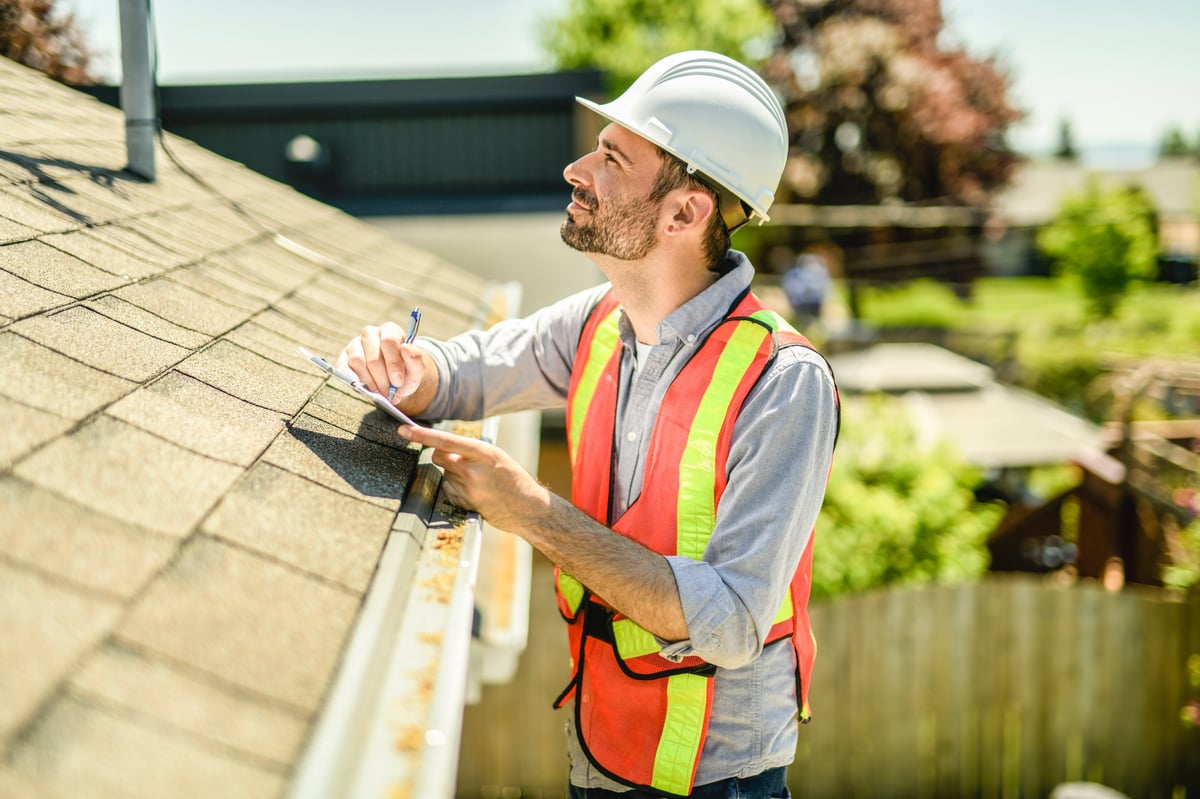 Inspector in a white hard hat holding a clipboard examining a house