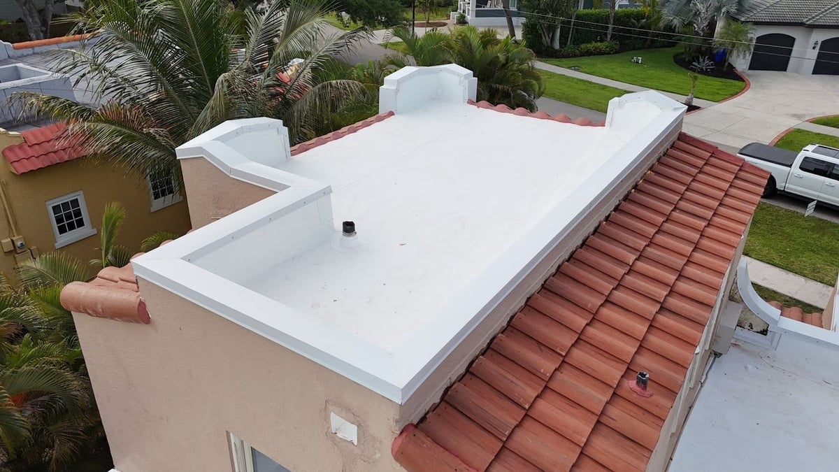 Close-up of a white flat roof membrane with white metal parapet coping, flashed pipe vent, and red clay barrel tile slope