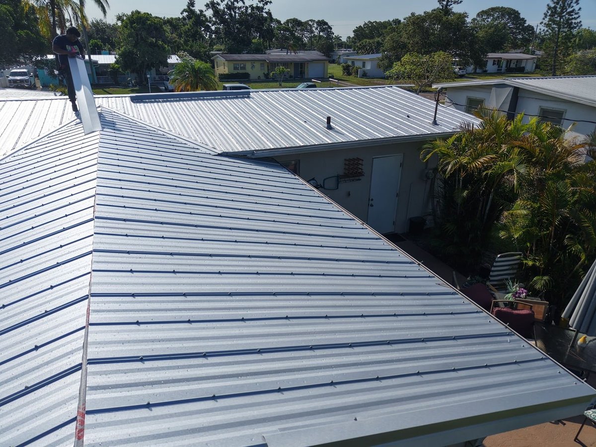 Silver metal roof hip ridge on a home with palm trees and the neighborhood in the background