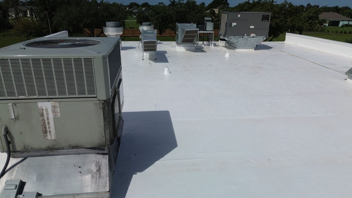 Close-up of a white membrane commercial roof with sealed pipe boots and seams beside rooftop HVAC units