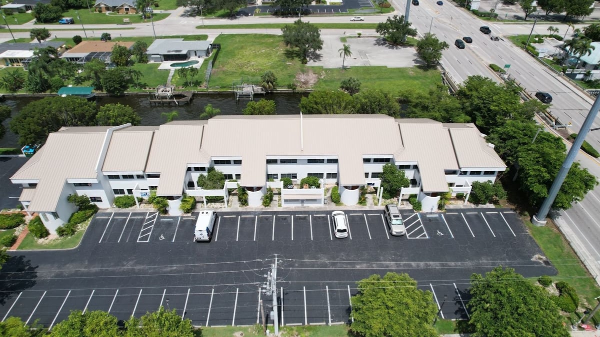 Aerial view of a commercial plaza and parking lot with a new tan standing seam metal roof in Cape Coral, FL