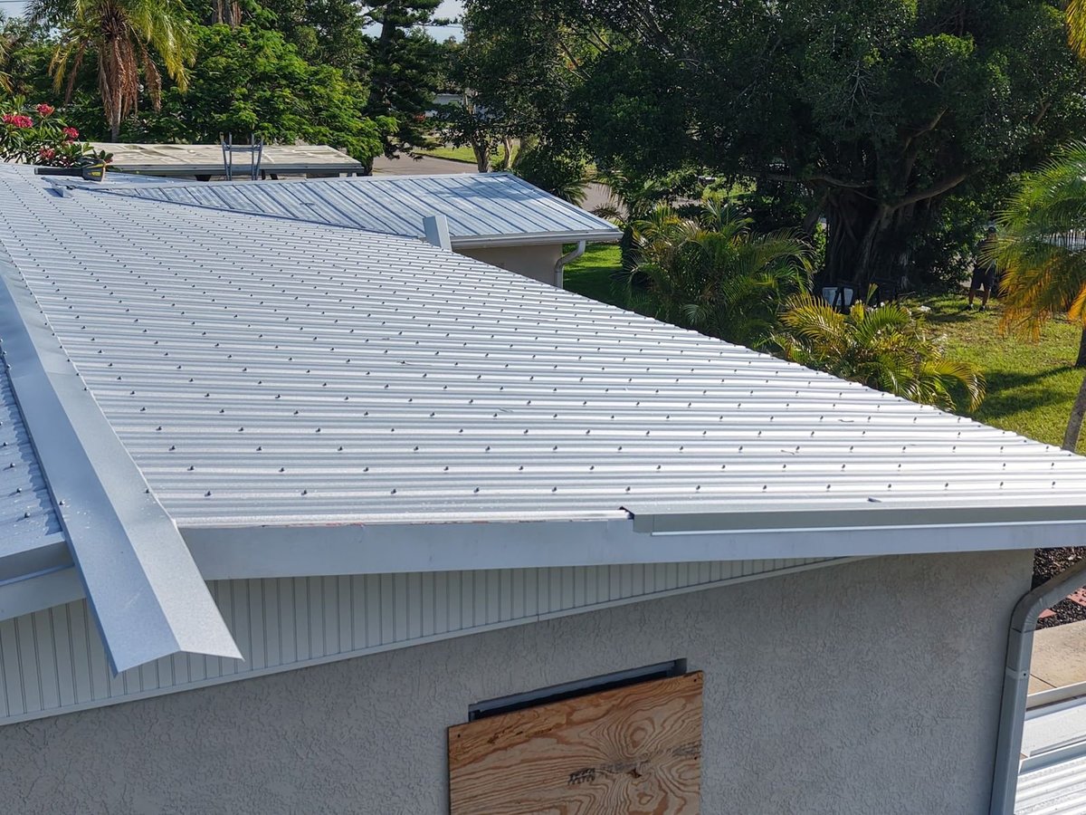 Silver exposed-fastener metal roof panels with new ridge and edge trim on a stucco home