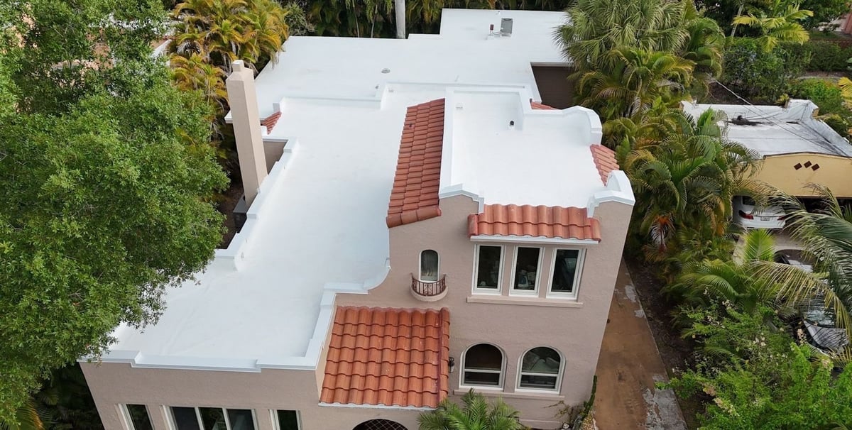 Aerial view of a Mediterranean-style home with a new white flat roof membrane and red clay barrel tile accents