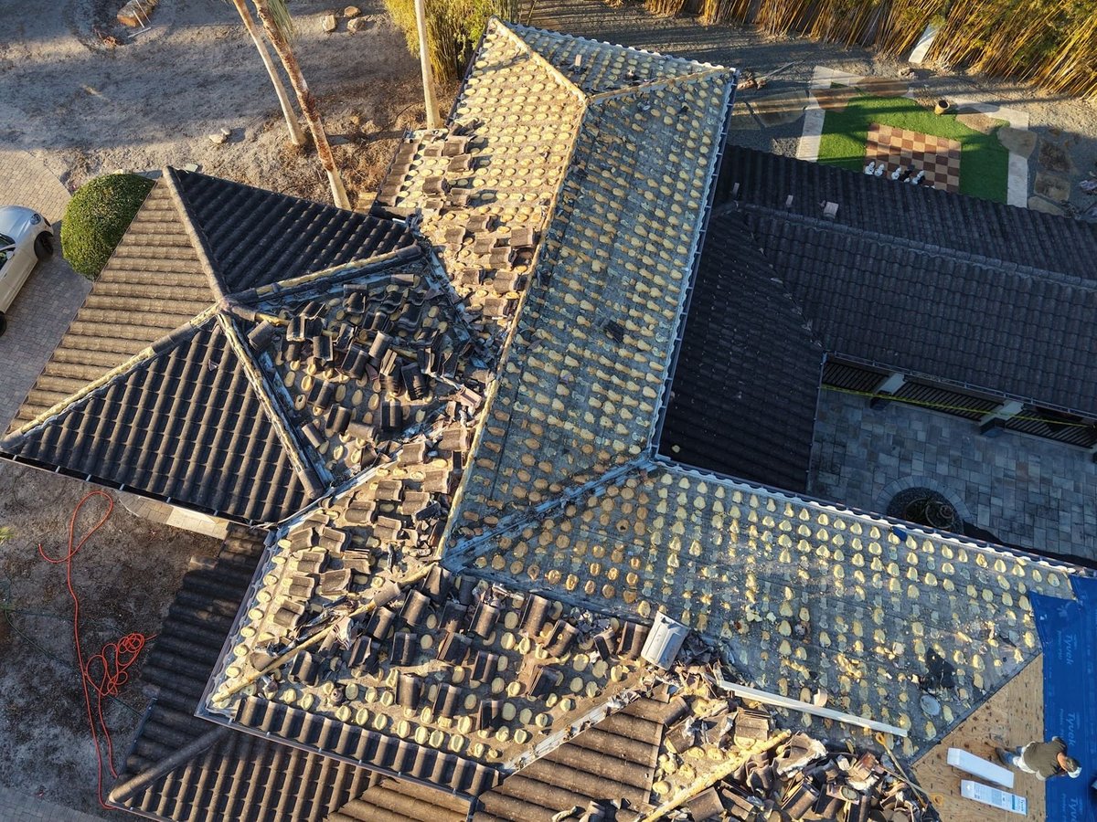 Close-up of a tile roof tear-off showing foam tile adhesive pads left on the old underlayment