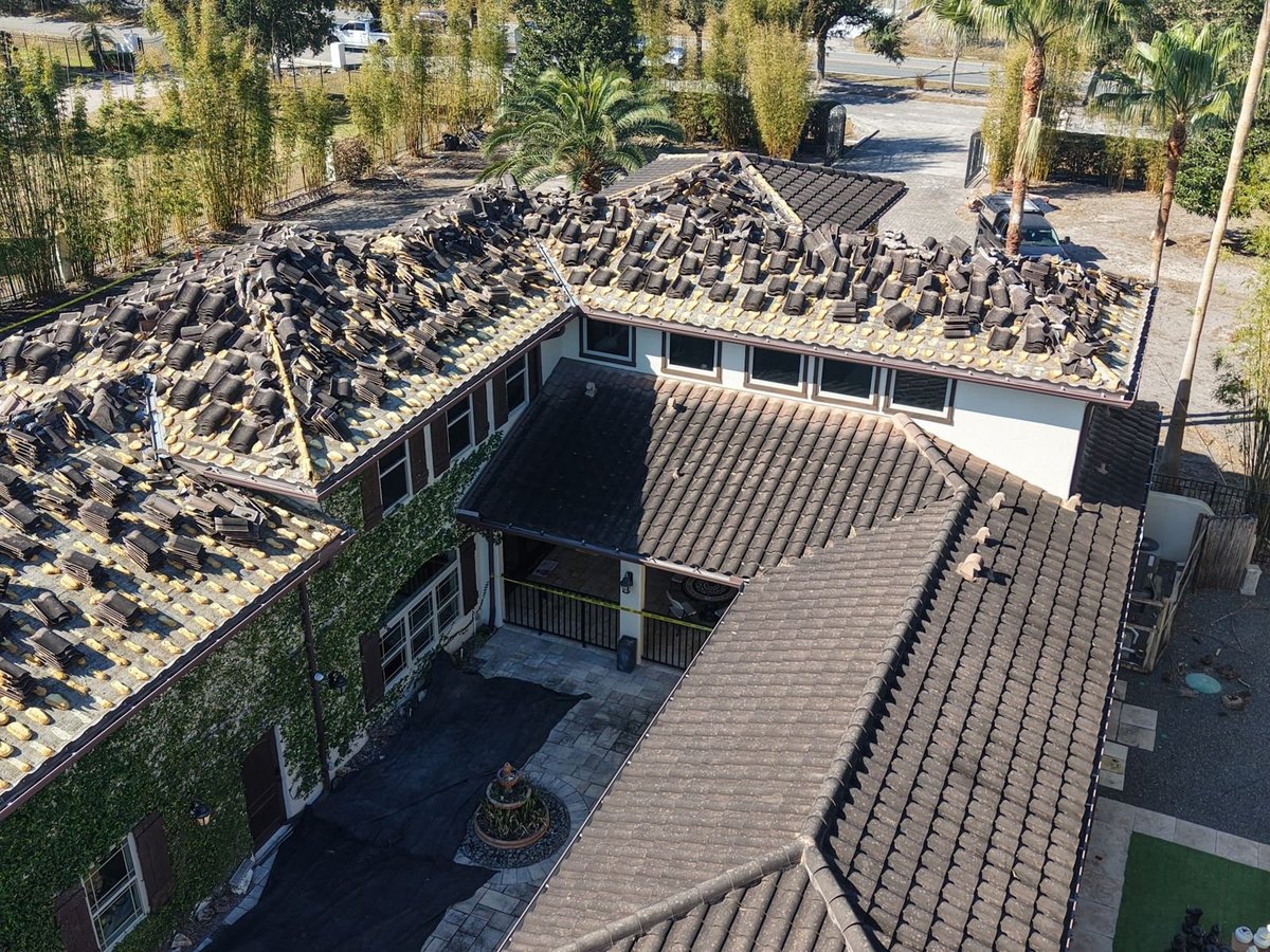 Old concrete tiles loosened and stacked on a roof during tile removal, next to sections of intact original tile