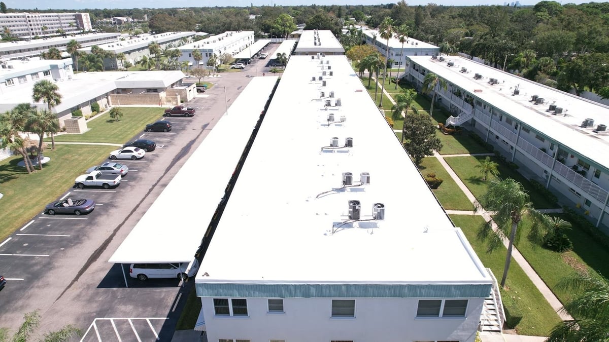 New white TPO roof on a long two-story residential building with rooftop AC units and covered parking