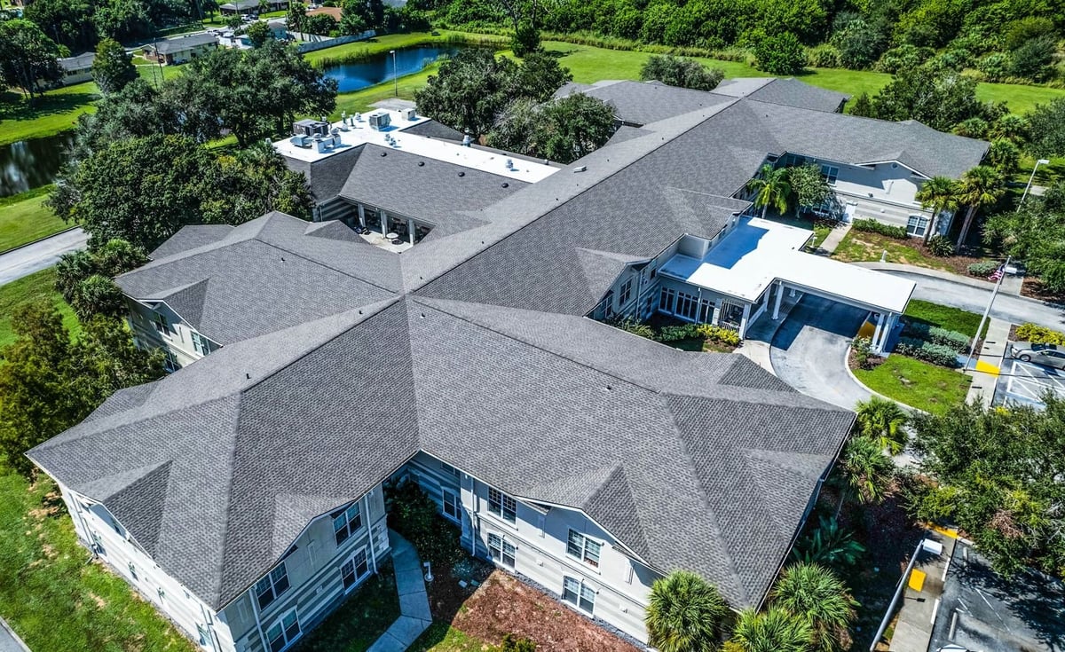 Aerial view of an assisted living facility with a new gray architectural shingle roof and white flat roof sections