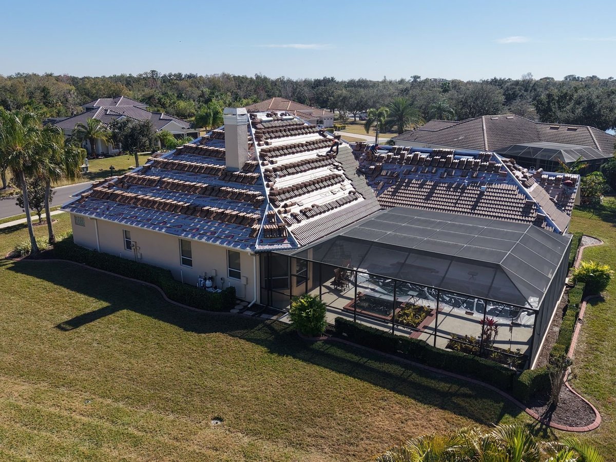 Hip tile roof replacement in progress: concrete tiles stacked on underlayment above a screened pool enclosure