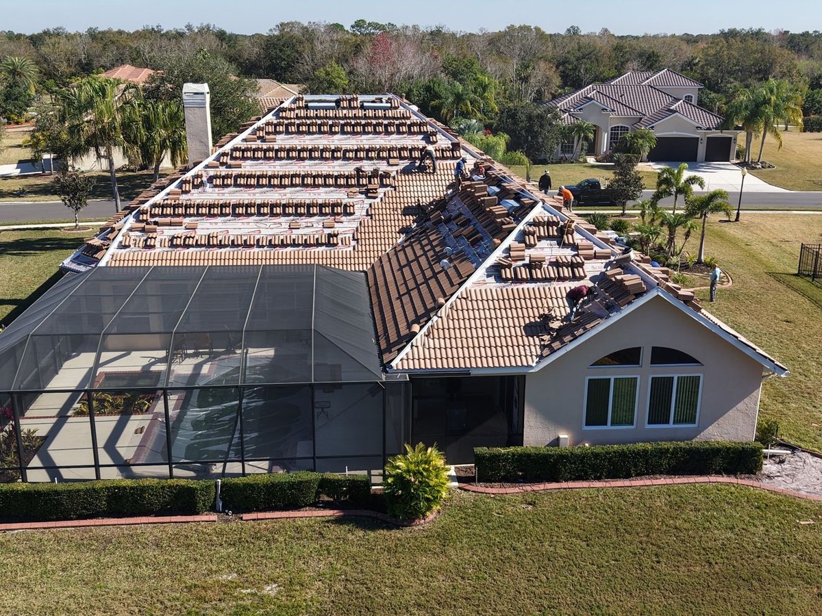 Roofers installing concrete barrel tile over new synthetic underlayment on a Florida pool home with a screened lanai