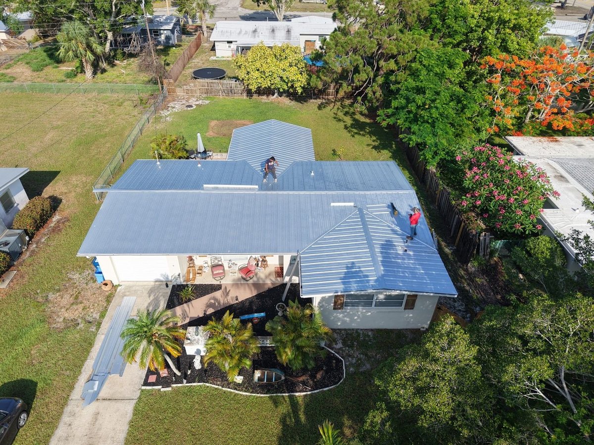 Aerial view of a crew installing a silver ribbed metal roof on a single-story Florida home
