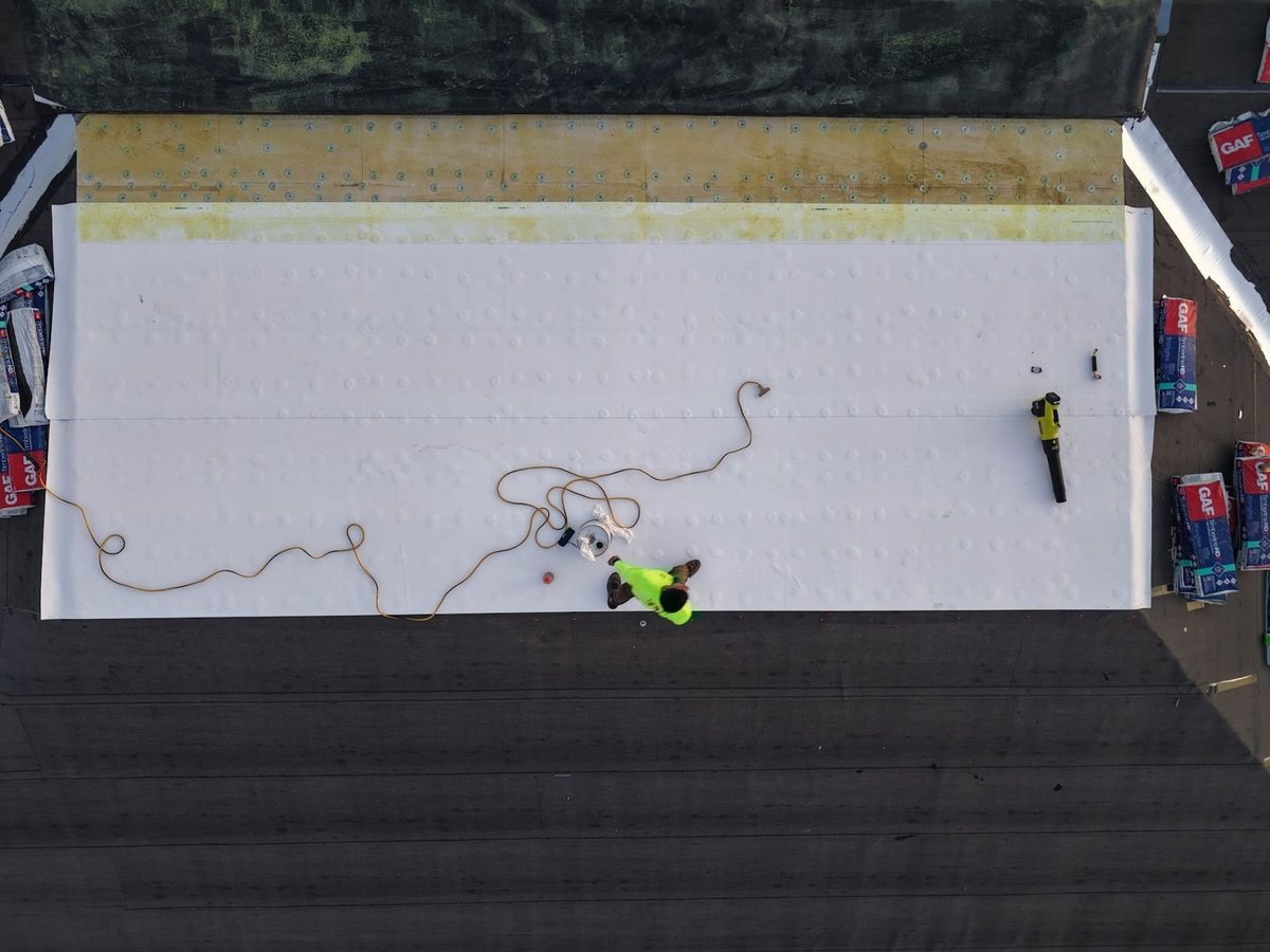 Crew tearing off old shingles down to the wood decking on a canal-side roof next to a flat roof section
