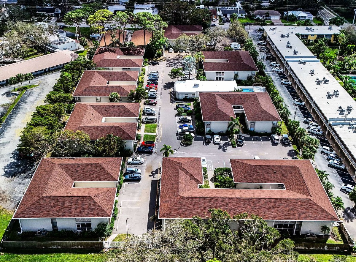 Aerial view of a residential neighborhood with multiple single-story homes featuring terracotta tile roofs arranged around a central courtyard with parked cars and landscaping