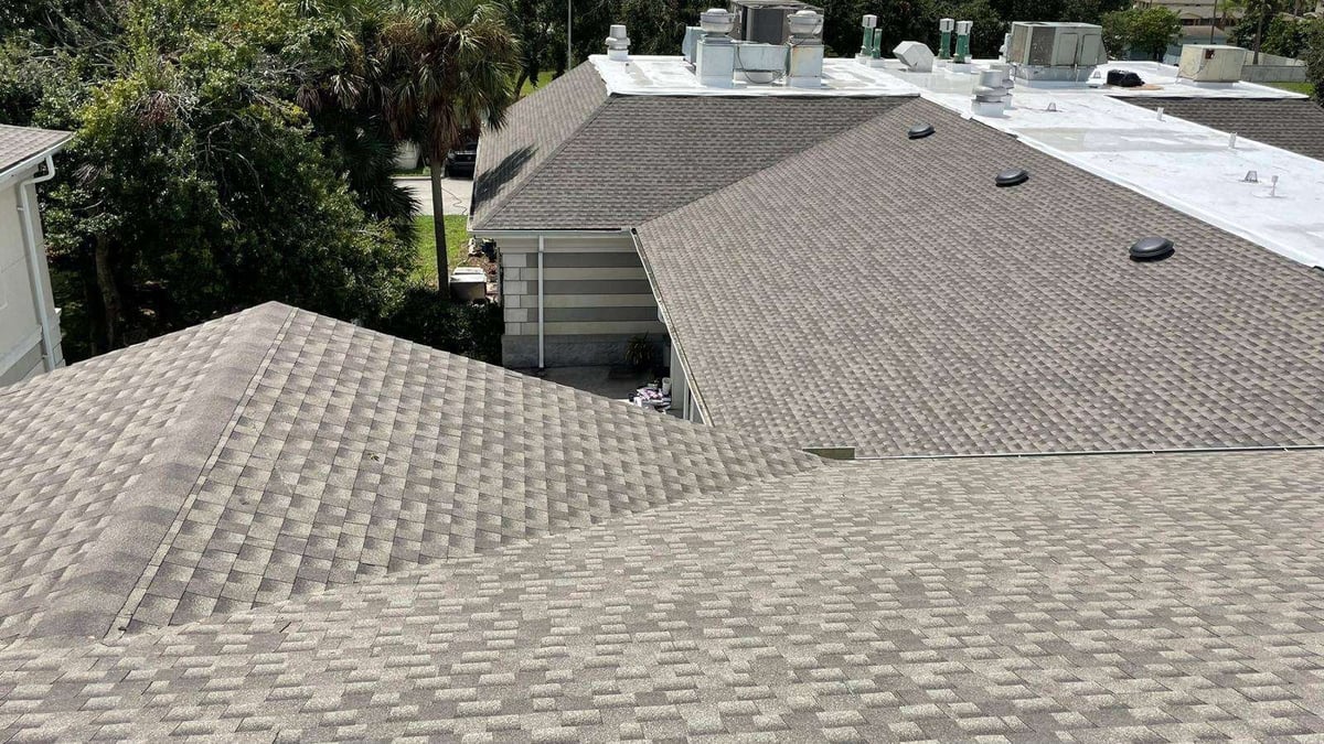 Aerial view of multiple residential roofs with asphalt shingles and HVAC units, showing rooflines and surrounding trees