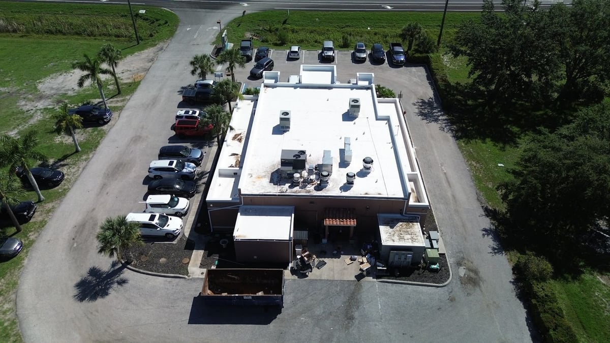 Overhead view of a restaurant's stained flat roof and roll-off dumpster at the start of a roof replacement