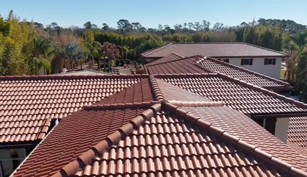 Aerial view of a large residential house with red terracotta tile roofing surrounded by trees and green landscape