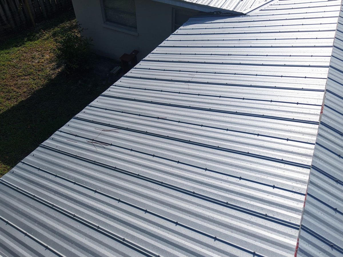 Close-up of new silver ribbed metal roof panels and fastener rows on a residential roof