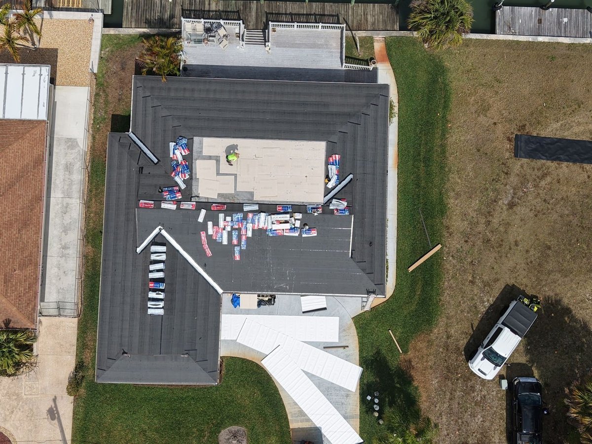 Roofers starting a shingle roof tear-off on a brown asphalt shingle roof, new bundles staged on the ridge